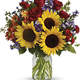 Bouquet of sunflowers, red roses, and purple flowers in a glass vase