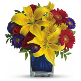 Bouquet of yellow lilies, red roses, and purple daisies in a blue glass vase