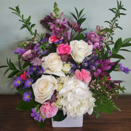 Mixed bouquet of white roses, hydrangea, and pink-purple flowers in a white vase