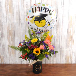 Tall mixed flower arrangement in a black vase with a 'Happy Graduation' balloon
