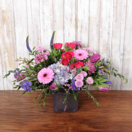 Low pink and purple mixed flower arrangement in a frosted purple glass cube vase