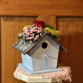 Small birdhouse topped with a red rose and pink flowers