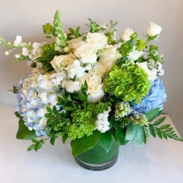 White roses and blue hydrangeas in a green glass vase