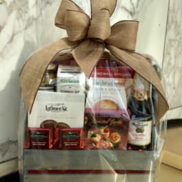 Gift basket with snacks, chocolates, and a bottle, wrapped in clear plastic with a large bow