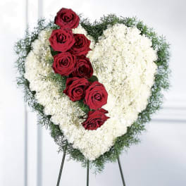 Heart-shaped floral tribute with red roses and white flowers on an easel