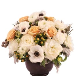Low arrangement of white ranunculus and anemones with peach roses in a dark round bowl vase