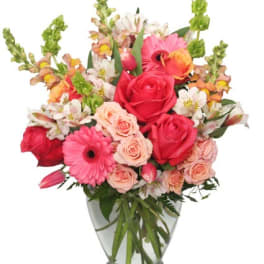 Mixed bouquet of pink roses, gerbera daisies, and peach spray roses in a clear glass vase