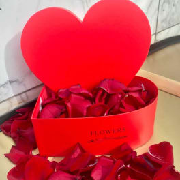 Red heart-shaped gift box filled with rose petals