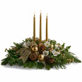 Low evergreen centerpiece with white flowers, pinecones, gold ornaments, and three tall gold taper candles.