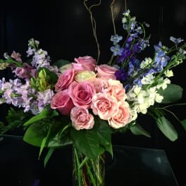 Glass vase arrangement of pink roses with lavender stock and blue delphinium