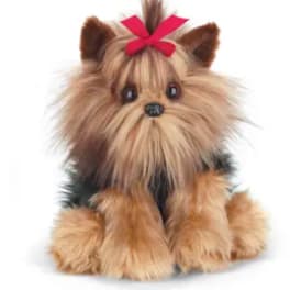 Small plush dog with long tan and black fur and a red bow on its head