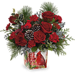 Red roses and carnations in a glass vase with pinecones and evergreen accents