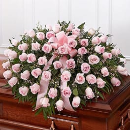 Pink rose casket spray with ribbon on a wooden casket