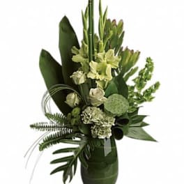 Tall green and white arrangement with roses, carnations, and tropical greenery in a green glass vase