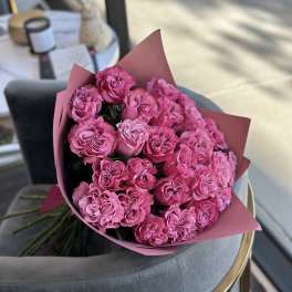 Large bouquet of bright pink roses wrapped in pink paper resting on a gray chair