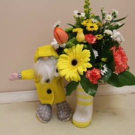 Yellow gerbera bouquet in a striped boot vase beside a small gnome figurine