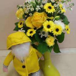Yellow rose and daisy bouquet in a vase beside a small gnome figurine.