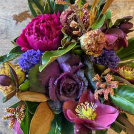 Purple and magenta floral bouquet with mixed blooms and broad leaves