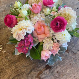 Round bouquet of pink, white, and peach flowers on a wooden surface