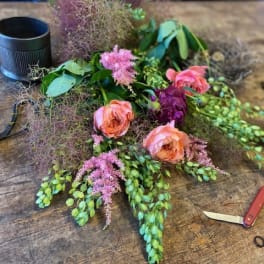 Loose floral arrangement with pink roses and purple blooms on a wooden table