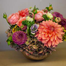 Mixed bouquet of pink, peach, and purple flowers in a low bowl vase
