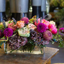 Low floral arrangement with pink, peach, and purple blooms in a glass vase