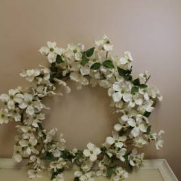 White floral wreath with green leaves on a neutral wall