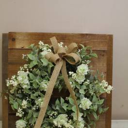 White floral wreath with a burlap bow on a wooden board