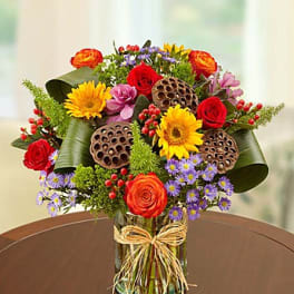 Mixed bouquet of roses, sunflowers, and purple daisies in a glass vase