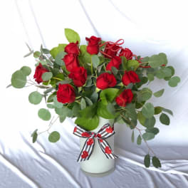 Red roses in a white vase with eucalyptus and a striped ribbon bow
