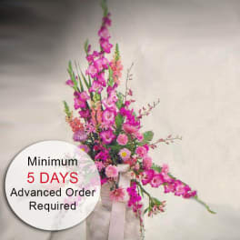 Tall pink floral arrangement with gladiolus and mixed flowers in a fabric-wrapped container