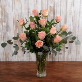 Arrangement of peach-pink roses with eucalyptus in a tall clear glass vase