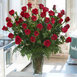 Large arrangement of red roses in a tall clear glass vase on a table