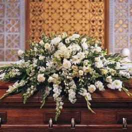 Large white floral casket spray arranged on a polished wooden coffin