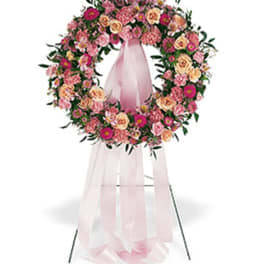 Standing wreath of pink and peach flowers with long pink ribbons on a metal easel