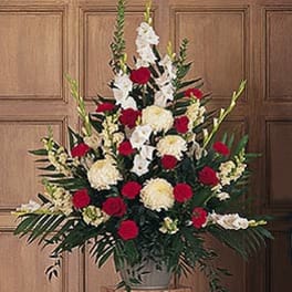 Tall arrangement of red roses, white gladiolus, and cream flowers in an urn-style vase.