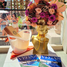 Gold bust vase with a pink and purple floral arrangement beside a clear bucket