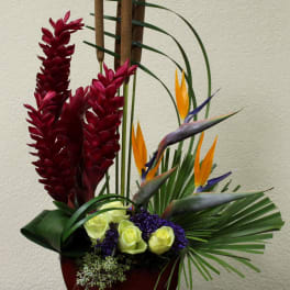 Tropical arrangement with red flowers, bird-of-paradise, and roses in a red vase