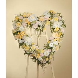 Heart-shaped standing wreath of white, yellow, and blush flowers on a wooden easel
