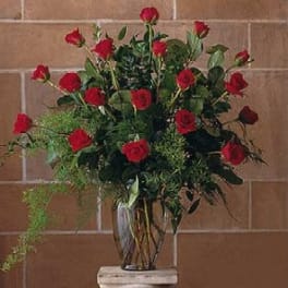 Tall arrangement of red roses with trailing greenery in a clear glass vase