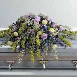 Pastel casket spray of lavender, yellow, blue, and green flowers on a silver casket