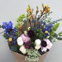 Mixed bouquet with blue, white, pink, and yellow flowers wrapped in brown paper