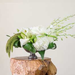 White floral arrangement in a silver pedestal bowl with long green stems