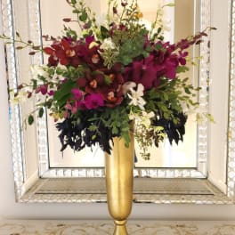 Tall floral arrangement in a gold vase with magenta, burgundy, and white orchids