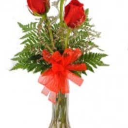 Three red roses in a clear glass vase with a red bow
