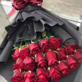 Bouquet of red roses wrapped in black paper with a pink ribbon