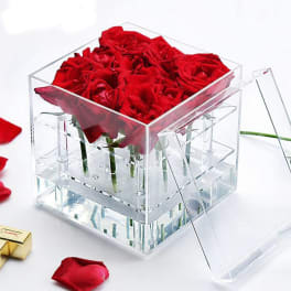 Red roses arranged in a clear acrylic box with a hinged lid.