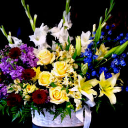 Tall mixed basket arrangement with yellow roses, lilies, white gladiolus, and blue delphinium.