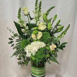 Tall arrangement of white roses, lilies, hydrangea, and green blooms in a glass cylinder vase