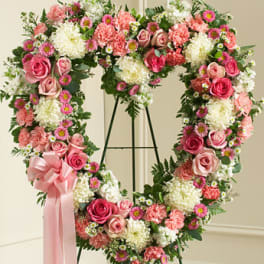 Heart-shaped floral wreath with pink roses and carnations on an easel